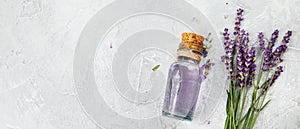 Bottle of essential oil and lavender flowers on light gray background