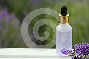Bottle of essential oil and lavender flowers on white wooden table in field, space for text