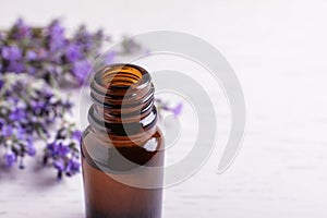 Bottle of essential oil and lavender flowers on white wooden background