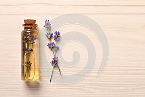 Bottle of essential oil and lavender flowers on white wooden table, flat lay. Space for text