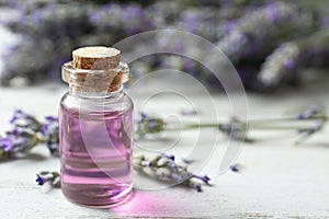 Bottle with essential oil and lavender flowers on wooden table. Space for text