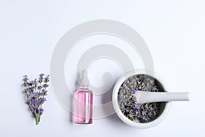 Bottle of essential oil, mortar and pestle with lavender flowers on white background