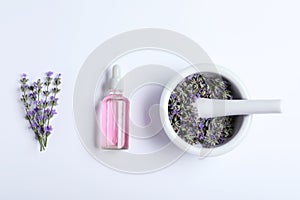 Bottle of essential oil, mortar and pestle with lavender  on white background, flat lay