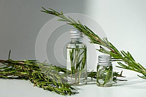 A bottle with essential oil and rosemary on a white background. A bottle of essential oil with fresh rosemary sprigs.