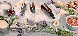 Bottle of essential oils with herbs and flowers on light gray background