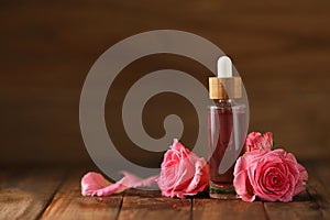 Bottle of essential rose oil and flowers on wooden table, space for text