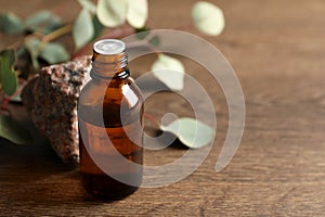 Bottle of eucalyptus essential oil, stone and leaves on wooden table. Space for text