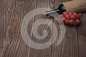 A bottle of expensive red wine and grapes lie on a background of wooden boards