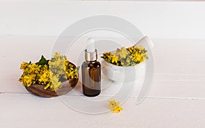 a bottle with face serum, healing natural St. John's wort oil on a white wooden background with the flowers of the