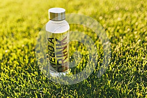 Bottle with fresh clean clear transparent water with text inscription I need drink on green grass on sunshine lawn