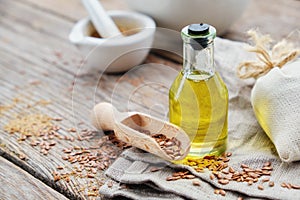 Bottle of fresh linseed oil, wooden scoop of flax seeds on linen cloth. Mortar on background