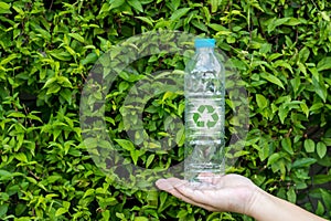 Bottle of fresh water on green tree wall. Hand holding plastic water bottle in concept recycle save the earth and environment