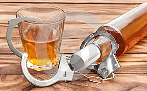 Bottle and glass with alcohol drink and handcuffs on wooden table. Alcohol dependence