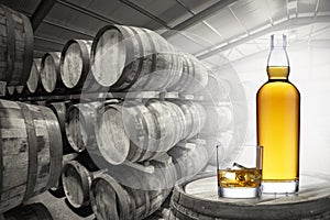 A bottle and glass of amber whisky set on top of an old barrel, in a barrel warehouse which is in black and white, back lit