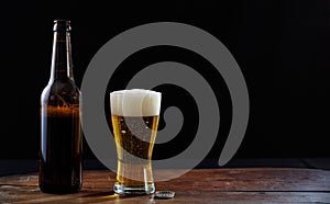 A bottle and a glass of beer on a wooden table, dark background