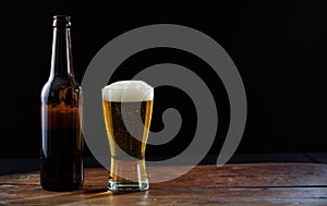 A bottle and a glass of beer on a wooden table, dark background