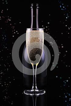 Bottle and glass of champagne on black background with golden bokeh circles. Place for text.Festive concept