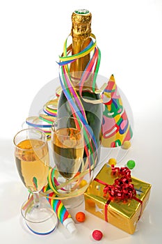 Bottle and glass of champagne, paper ribbon, confetti, party hats and gifts on white background