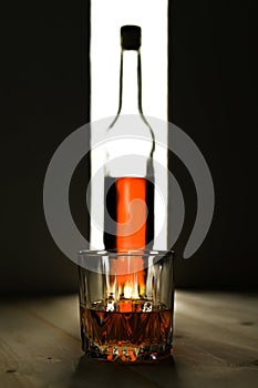 Bottle and glass of cognac over dark and white background