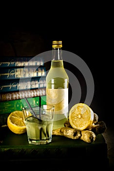 Bottle and glass with craft lemon-ginger alchol drink on background with books