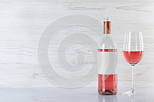 Bottle and glass of delicious rose wine on table against white wooden background. Space for text