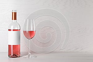 Bottle and glass of delicious rose wine on table against white wooden background. Space for text