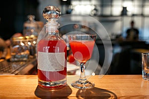 Bottle and glass filled with red alcoholic drink on the bar counter