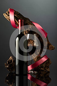 Bottle and glass of red wine on a black reflective background