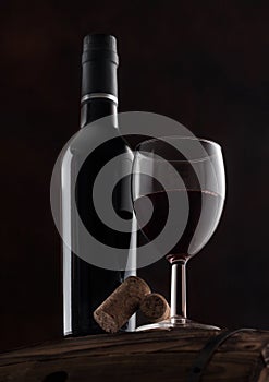 Bottle and glass of red wine with corks and vintage corkscrew on top of wooden barrel on black