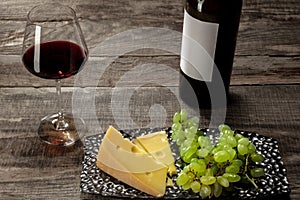 A bottle and a glass of red wine with fruits over wooden background