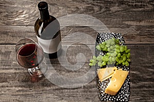 A bottle and a glass of red wine with fruits over wooden background