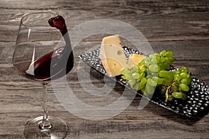 A bottle and a glass of red wine with fruits over wooden background