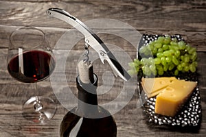 A bottle and a glass of red wine with fruits over wooden background