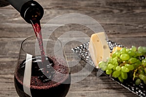 A bottle and a glass of red wine with fruits over wooden background