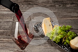 A bottle and a glass of red wine with fruits over wooden background