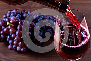 Bottle and glass of red wine, grape and cork on wooden background