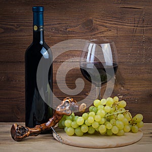 Bottle and glass of red wine, grapes and corkscrew made of grapevine
