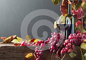 Bottle and glass of red wine and grapes with vine leaves on a old wooden table