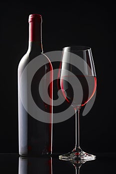 A bottle and a glass of red wine stand on a black mirror table