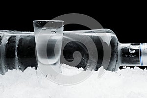 Bottle with glass of vodka lying on ice on black background