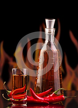 Bottle, glass vodka, red hot chili pepper on background flames.