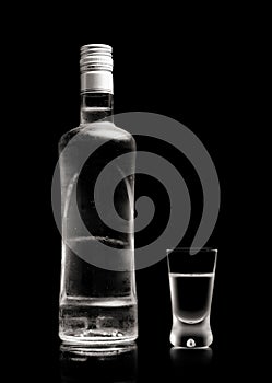 Bottle and glass of vodka standing isolated on black