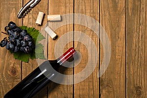 Bottle and glass with wine bunches of grapes and vine leaves on wooden background. Top view with copy space