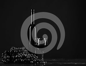 Bottle and glass of wine on dark brown background. Winetasting and degustation still life concept. Bordeaux or cabernet