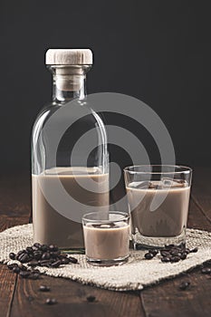 Bottle and glasses of Cream coffee liqueur with ice, and coffee  beans on rustic wooden background