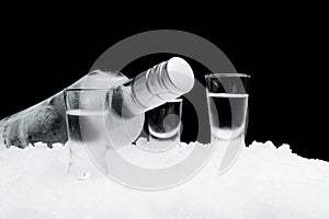 Bottle with glasses of vodka lying on ice on black background