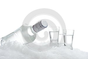 Bottle and glasses of vodka lying on ice on white