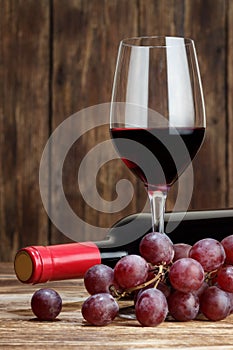 Bottle, grape and glass of red wine on wooden background