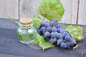 Bottle with grape seed oil and blue grapes on a wooden table