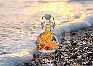The bottle of Greek olive oil on the sea stony beach in the sea foamy wave